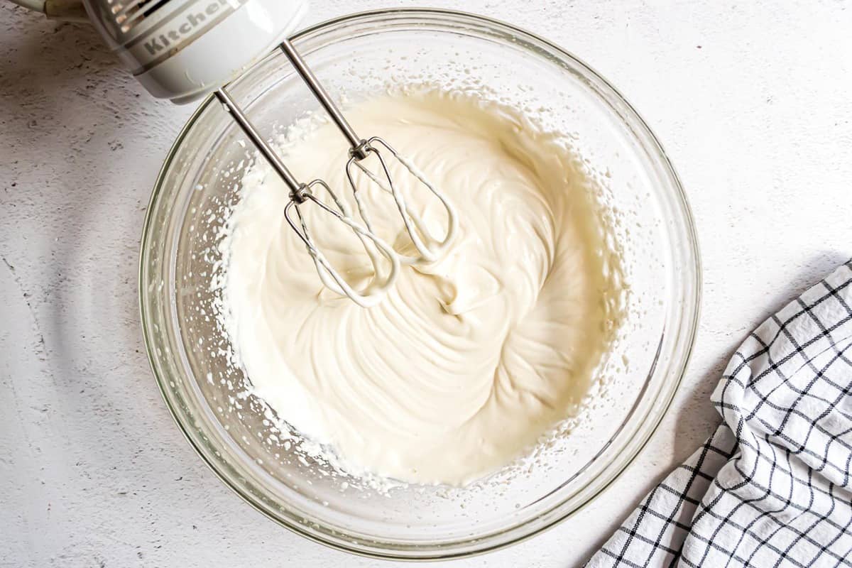 Relleno de mascarpone en un tazón de mezcla de vidrio transparente con batidora eléctrica.