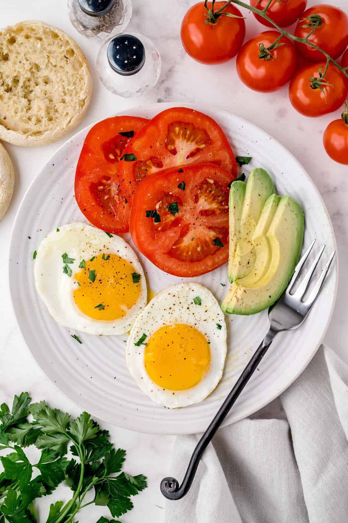 Plato de comida para el desayuno incluyendo huevos fritos por el lado soleado, tomates, aguacate.