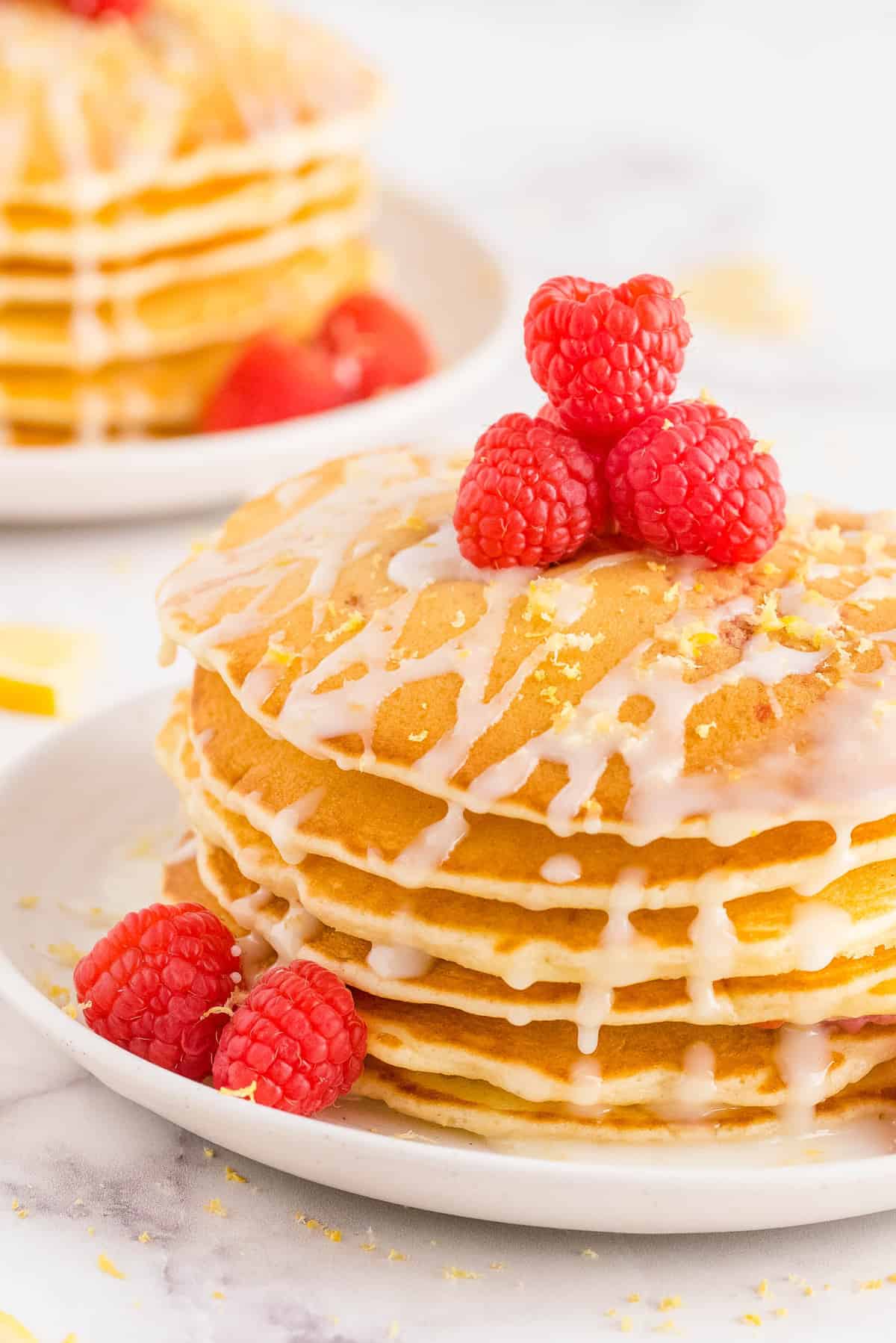 堆叠的煎饼，上面装饰着新鲜的覆盆子、柠檬糖霜和柠檬皮。